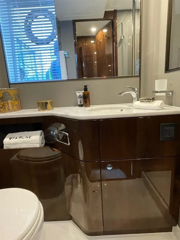 Modern bathroom featuring a sink, mirror, toiletries, a towel labelled 'FAIRLINE', and wooden accents.